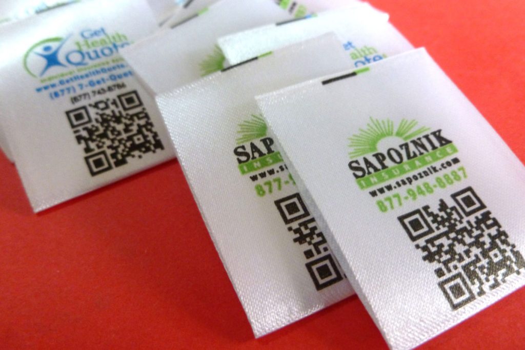 Etiquetas en satín doblado con marca y códigos QR con links de páginas web u otra información